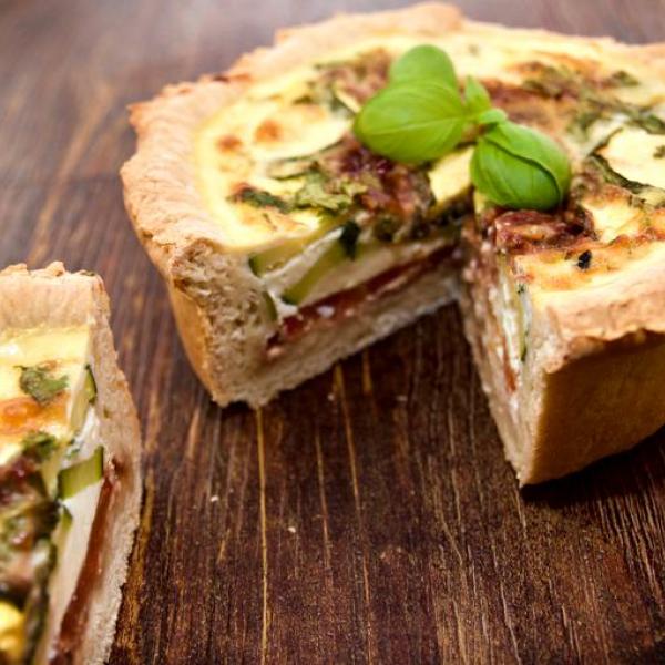 Un delicioso quiche mediterráneo de capas profundas con guarnición de albahaca.